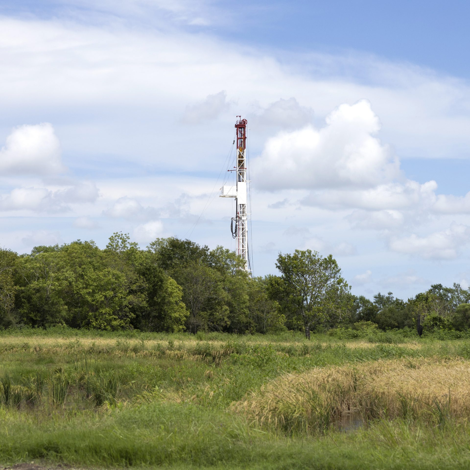 An oil rig behind green landscape and trees.