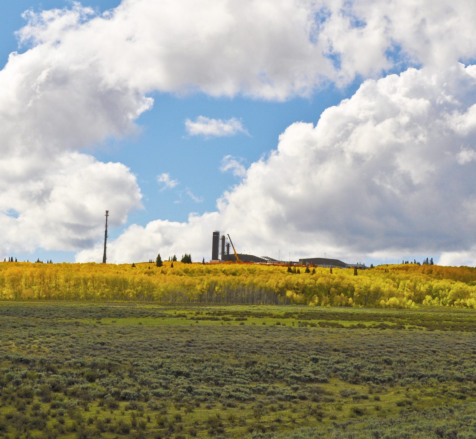 A green landscape with operations in the distance, under a blue sky.
